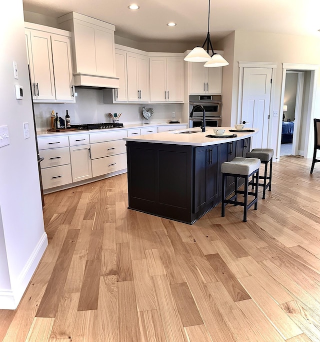 kitchen featuring hanging light fixtures, a kitchen island with sink, white cabinetry, and light hardwood / wood-style floors