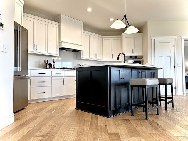 kitchen with white cabinetry, stainless steel appliances, a center island with sink, and decorative light fixtures