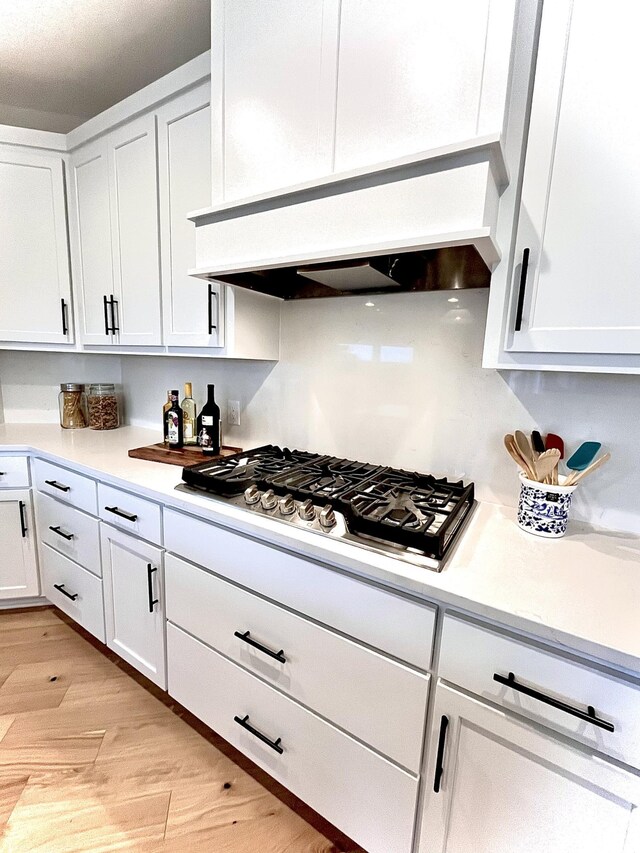 kitchen with light wood-type flooring, premium range hood, white cabinetry, and stainless steel gas cooktop