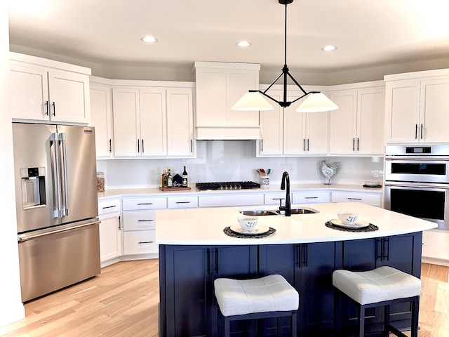 kitchen with decorative light fixtures, white cabinetry, appliances with stainless steel finishes, and a center island with sink