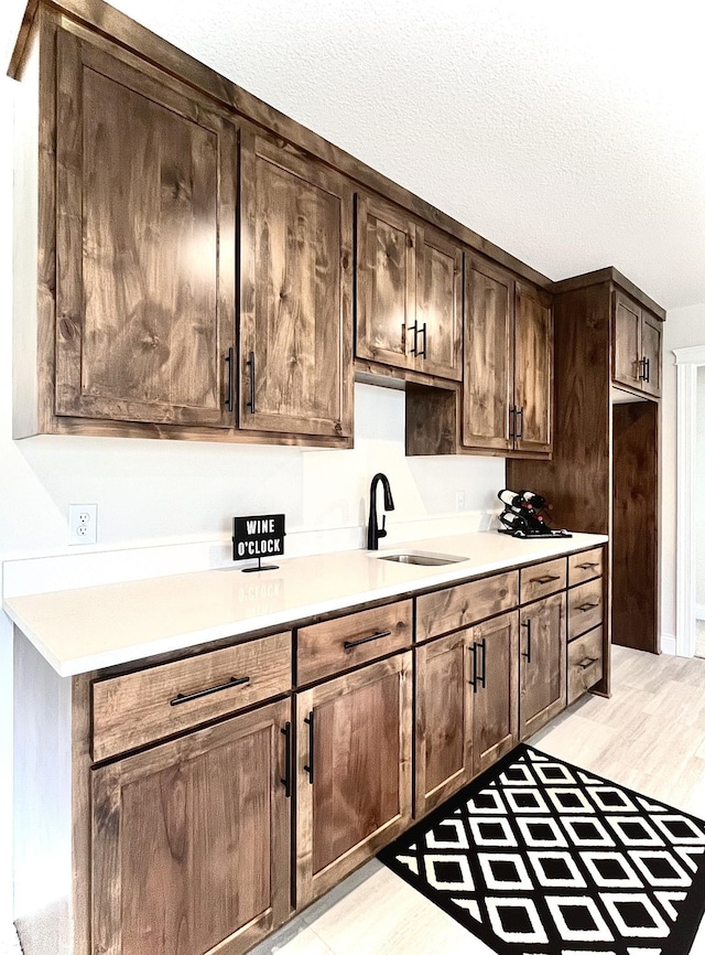 kitchen with a textured ceiling, light hardwood / wood-style flooring, dark brown cabinetry, and sink