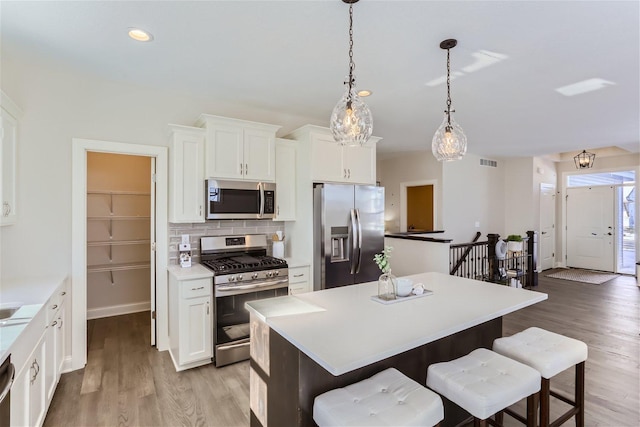 kitchen with pendant lighting, light hardwood / wood-style flooring, a breakfast bar, stainless steel appliances, and white cabinets