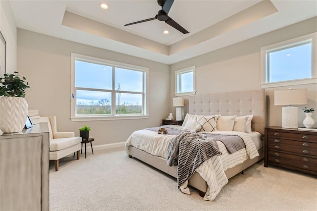 carpeted bedroom with multiple windows, a tray ceiling, and ceiling fan