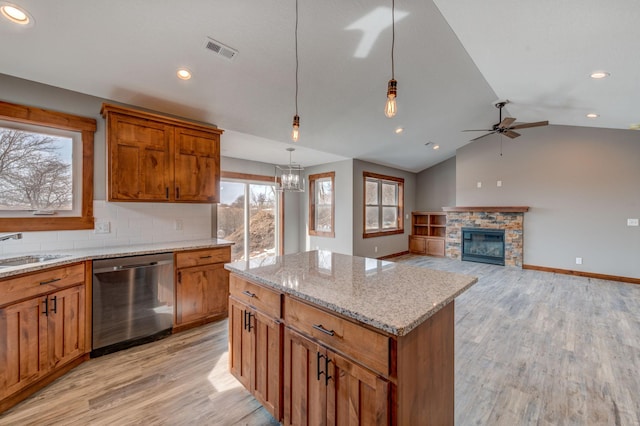 kitchen with decorative light fixtures, a center island, light wood-type flooring, dishwasher, and a fireplace