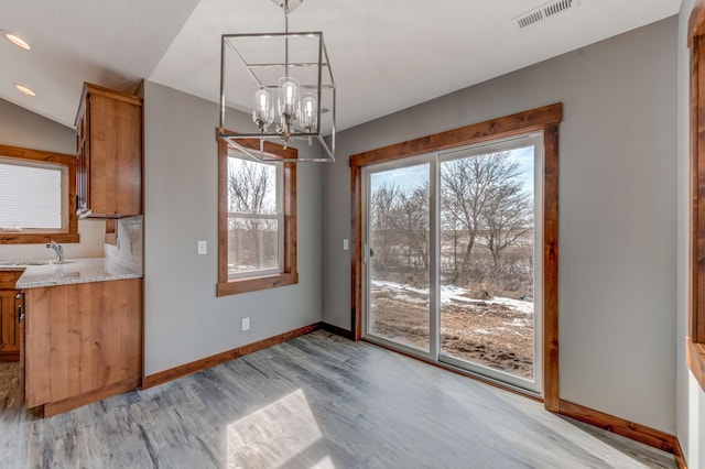 unfurnished dining area with sink, light hardwood / wood-style flooring, and a notable chandelier