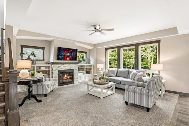 living room featuring vaulted ceiling, hardwood / wood-style floors, ceiling fan, and a stone fireplace