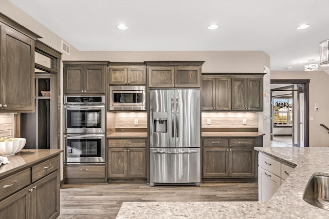 kitchen with light stone countertops, appliances with stainless steel finishes, light hardwood / wood-style floors, tasteful backsplash, and dark brown cabinetry