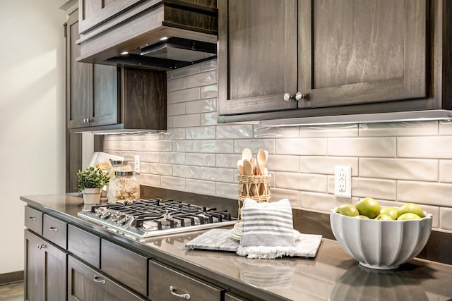 kitchen with stainless steel gas cooktop, premium range hood, decorative backsplash, and dark brown cabinetry