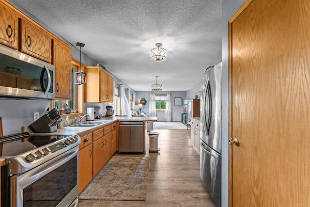 7702 County Road 5 NE, North Branch, MN 55056 - kitchen with stainless steel appliances, a peninsula, wood finished floors, hanging light fixtures, and a textured ceiling