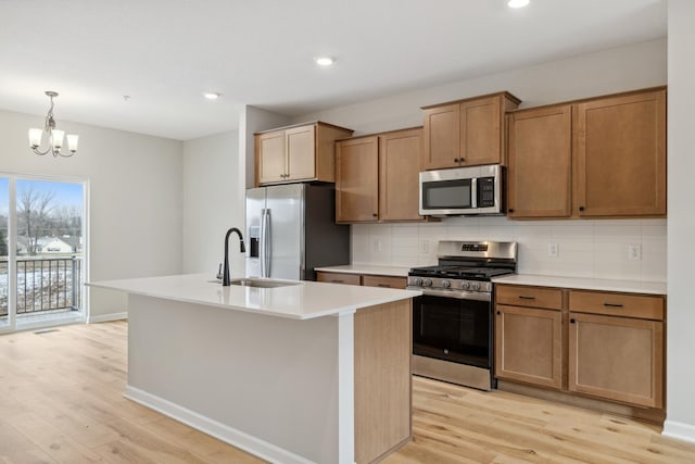 kitchen featuring sink, an island with sink, light hardwood / wood-style floors, stainless steel appliances, and a chandelier