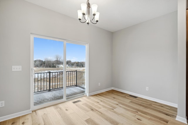 spare room with a chandelier and light wood-type flooring