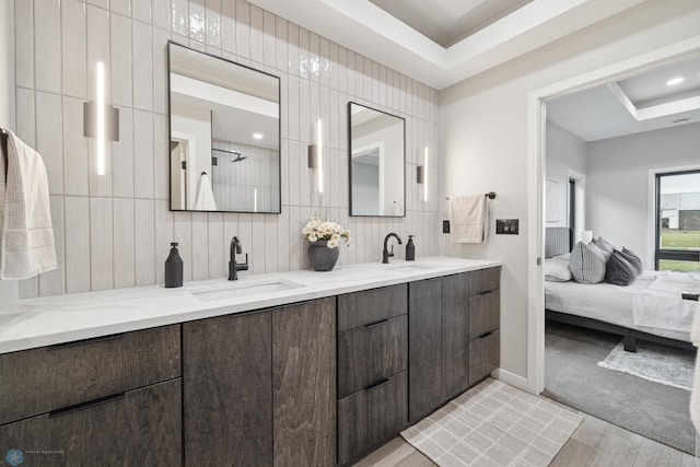 ensuite bathroom with double vanity, a sink, backsplash, and wood finished floors