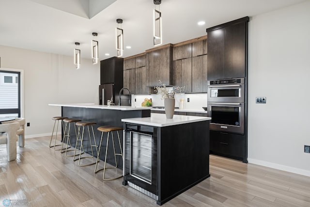 kitchen featuring beverage cooler, light countertops, light wood finished floors, and a center island with sink
