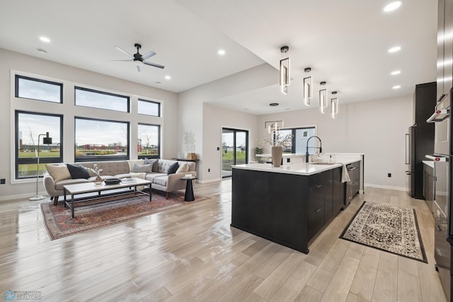 kitchen featuring ceiling fan, light countertops, dark cabinets, a kitchen island with sink, and open floor plan