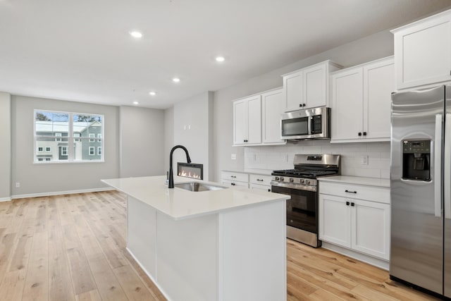 kitchen with light hardwood / wood-style floors, sink, stainless steel appliances, and a kitchen island with sink