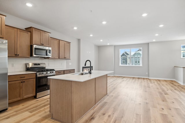 kitchen with a center island with sink, light wood-type flooring, sink, and appliances with stainless steel finishes