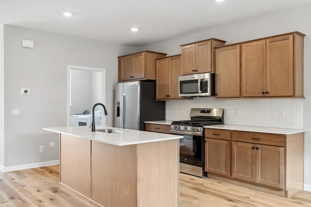 kitchen with sink, an island with sink, decorative backsplash, appliances with stainless steel finishes, and light wood-type flooring