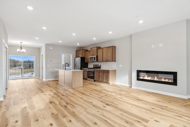 kitchen with appliances with stainless steel finishes, a center island with sink, light hardwood / wood-style flooring, and sink