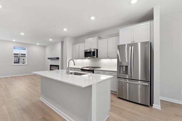 kitchen featuring a kitchen island with sink, white cabinets, sink, light hardwood / wood-style floors, and stainless steel appliances