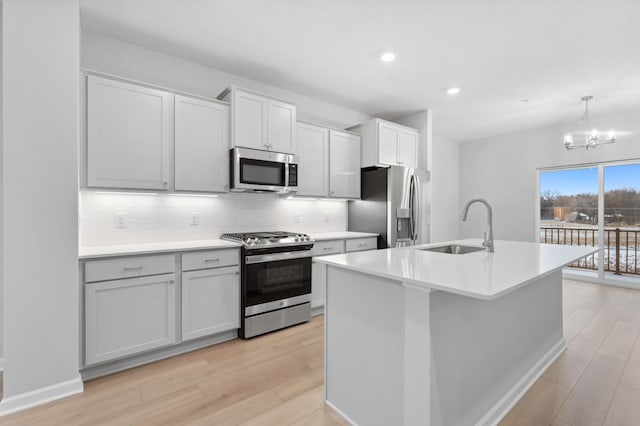 kitchen with sink, an island with sink, decorative light fixtures, appliances with stainless steel finishes, and light wood-type flooring