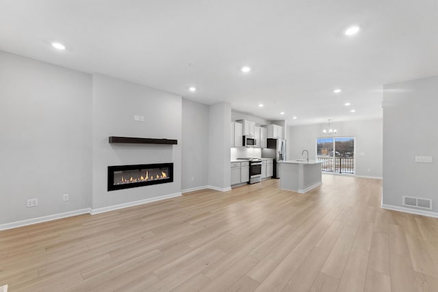 unfurnished living room with light hardwood / wood-style floors, sink, and a chandelier