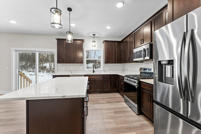 kitchen featuring a center island, sink, hanging light fixtures, dark brown cabinetry, and stainless steel appliances