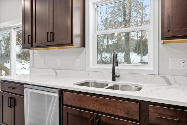 kitchen with dark brown cabinetry, light stone counters, stainless steel dishwasher, and sink