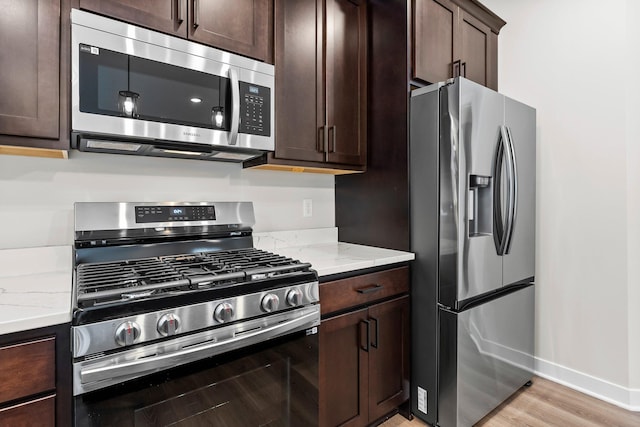 kitchen featuring dark brown cabinetry, light stone counters, light hardwood / wood-style flooring, and stainless steel appliances