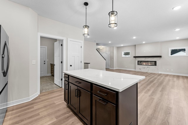 kitchen featuring stainless steel fridge, decorative light fixtures, dark brown cabinets, light wood-style floors, and a high end fireplace