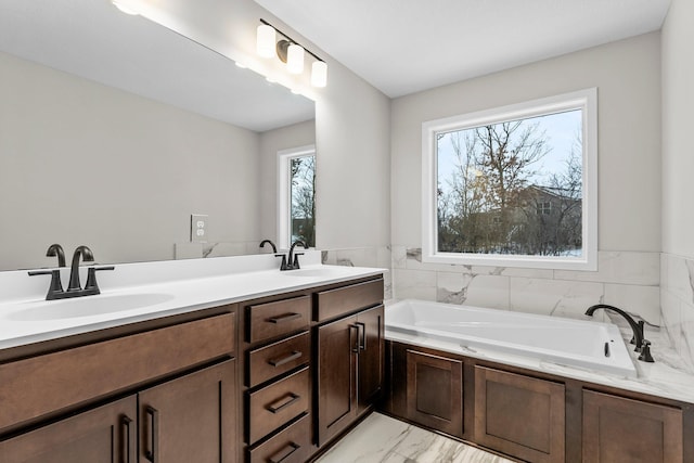 bathroom with double vanity, marble finish floor, a garden tub, and a sink