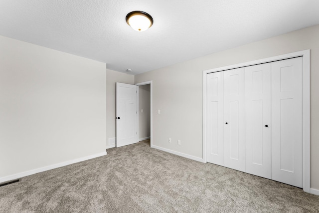 unfurnished bedroom with carpet, visible vents, a textured ceiling, and baseboards