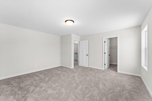 unfurnished bedroom with a walk in closet, carpet flooring, baseboards, and multiple windows