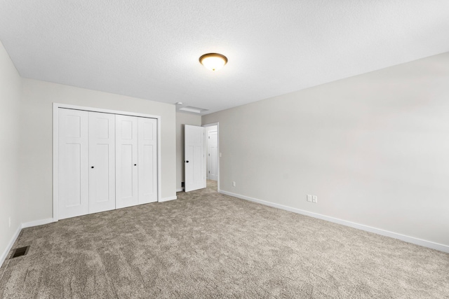 unfurnished bedroom with visible vents, baseboards, a textured ceiling, carpet floors, and a closet