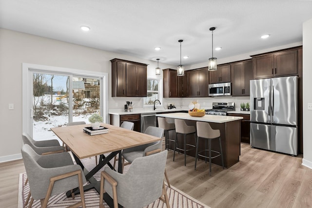 19498 Carson Ct NW, Elk River, MN 55330 - kitchen featuring stainless steel appliances, dark brown cabinets, light countertops, light wood finished floors, and a center island