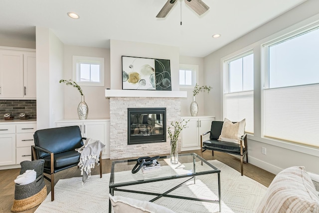 living area with ceiling fan, a stone fireplace, and light wood-type flooring