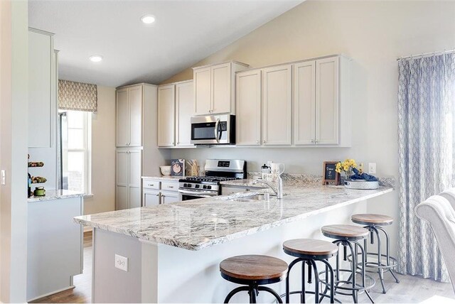 kitchen with a kitchen bar, stainless steel appliances, light wood-type flooring, and vaulted ceiling