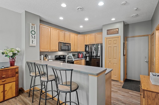 kitchen with light brown cabinets, light wood-type flooring, kitchen peninsula, and black appliances