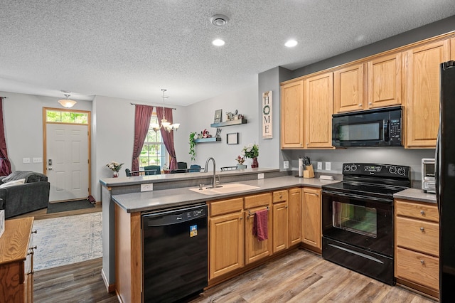 kitchen featuring a sink, light wood-type flooring, black appliances, and a peninsula