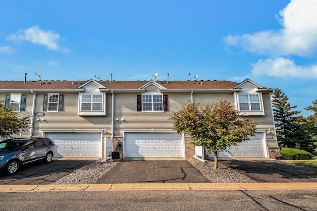 view of property with driveway, an attached garage, and central AC