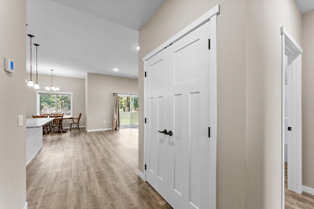 corridor featuring a textured ceiling, a healthy amount of sunlight, a notable chandelier, and light hardwood / wood-style floors