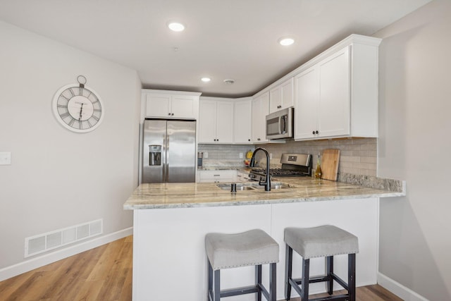 kitchen featuring appliances with stainless steel finishes, kitchen peninsula, white cabinetry, and light hardwood / wood-style flooring