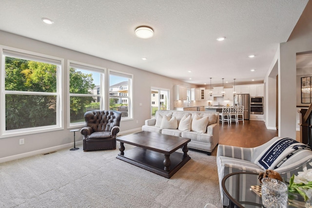 living area with recessed lighting, light colored carpet, a textured ceiling, and baseboards