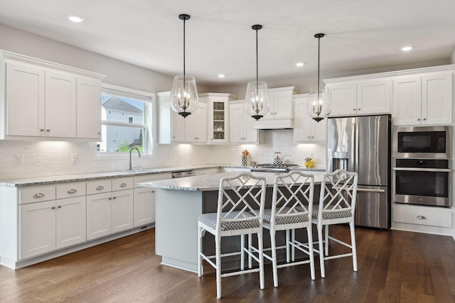 kitchen featuring a center island, pendant lighting, stainless steel appliances, glass insert cabinets, and white cabinets