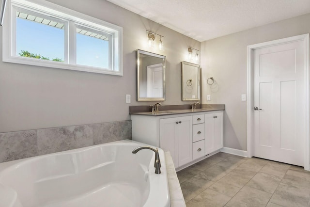 full bath featuring a garden tub, double vanity, a sink, a textured ceiling, and baseboards