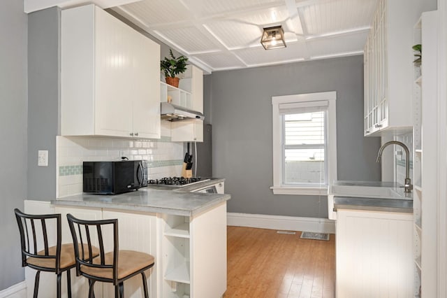 kitchen with white cabinetry, kitchen peninsula, a breakfast bar, light hardwood / wood-style flooring, and backsplash