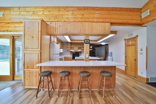 kitchen with visible vents, a breakfast bar, light countertops, freestanding refrigerator, and light wood-style floors