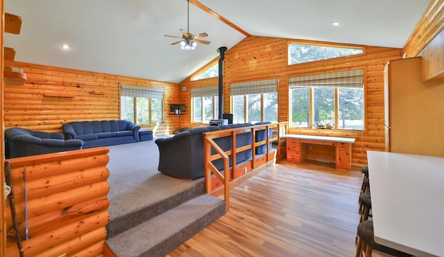 living area featuring a wealth of natural light, high vaulted ceiling, wood finished floors, and a wood stove