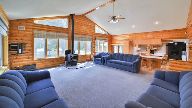 living area with visible vents, high vaulted ceiling, a wood stove, and carpet floors