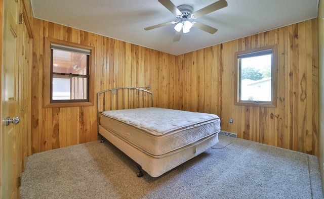 bedroom featuring a ceiling fan, wooden walls, carpet, and visible vents