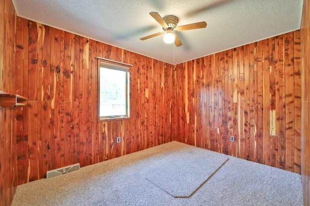 unfurnished room with wooden walls, a ceiling fan, visible vents, and a textured ceiling